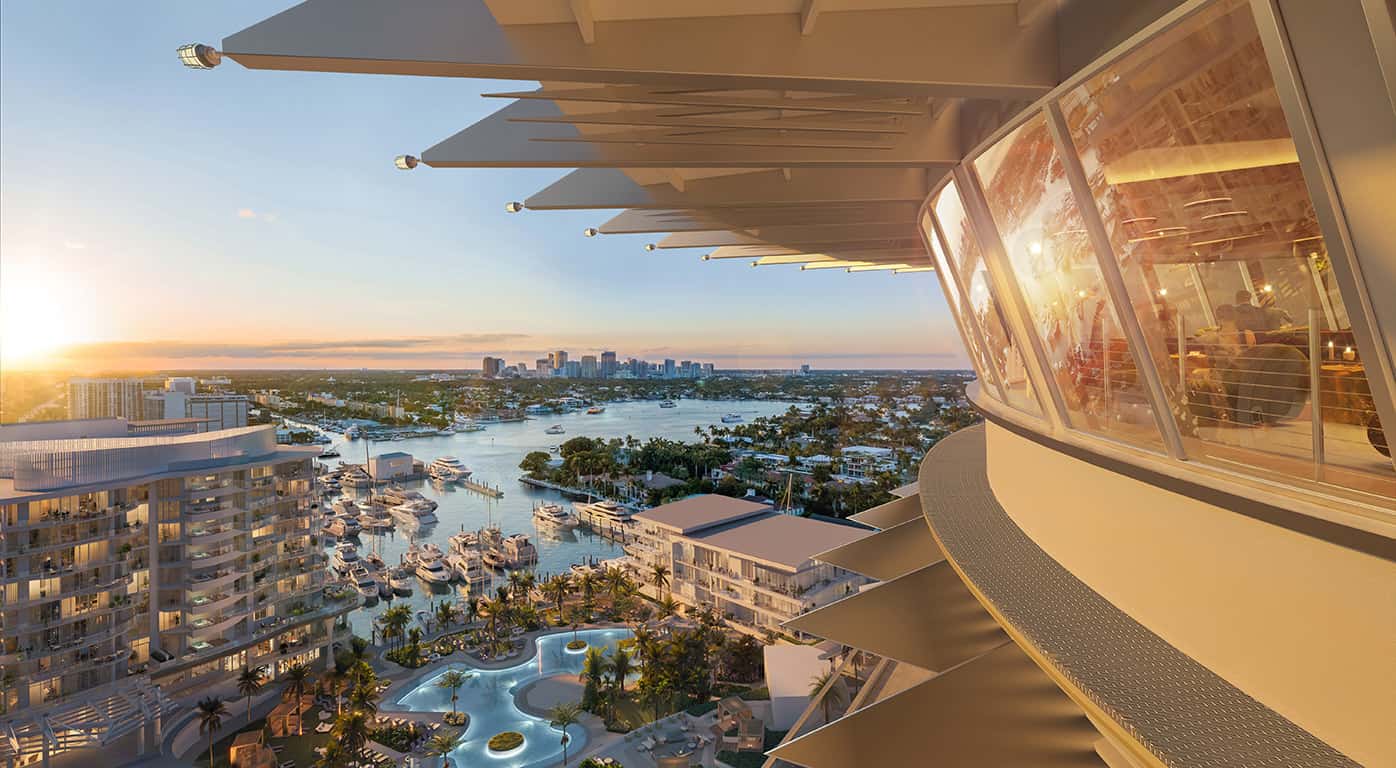 Aerial view of a waterfront resort with a marina of boats, palm trees, and a city skyline at sunset; a curved glass-walled restaurant extends from the right.