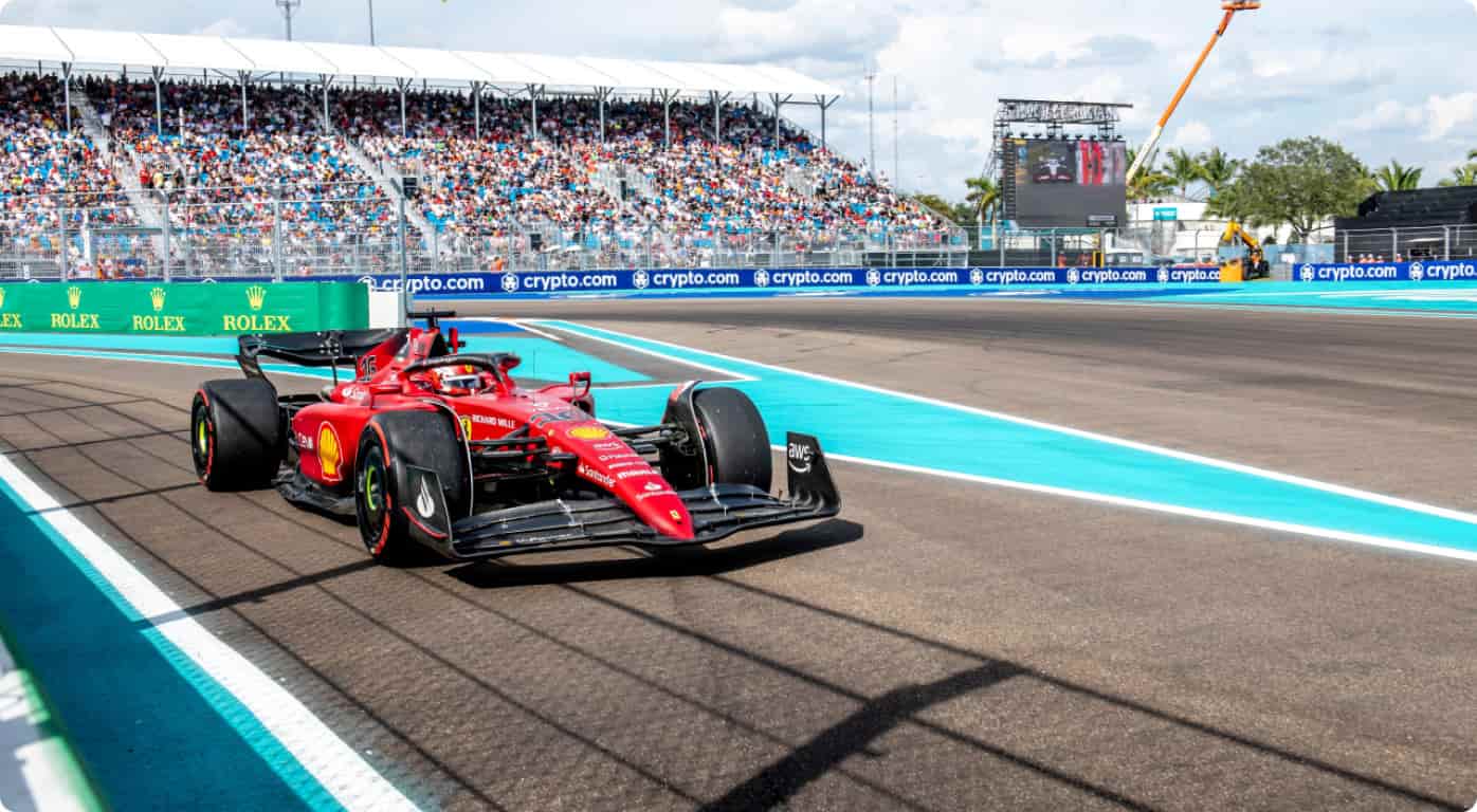 Red Ferrari Formula 1 car speeding along a race track with turquoise run-off and a packed grandstand behind Rolex banners.