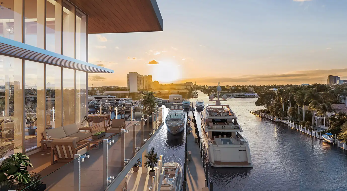 Sunset over a marina with luxury yachts docked along a canal, viewed from a glass-walled terrace.