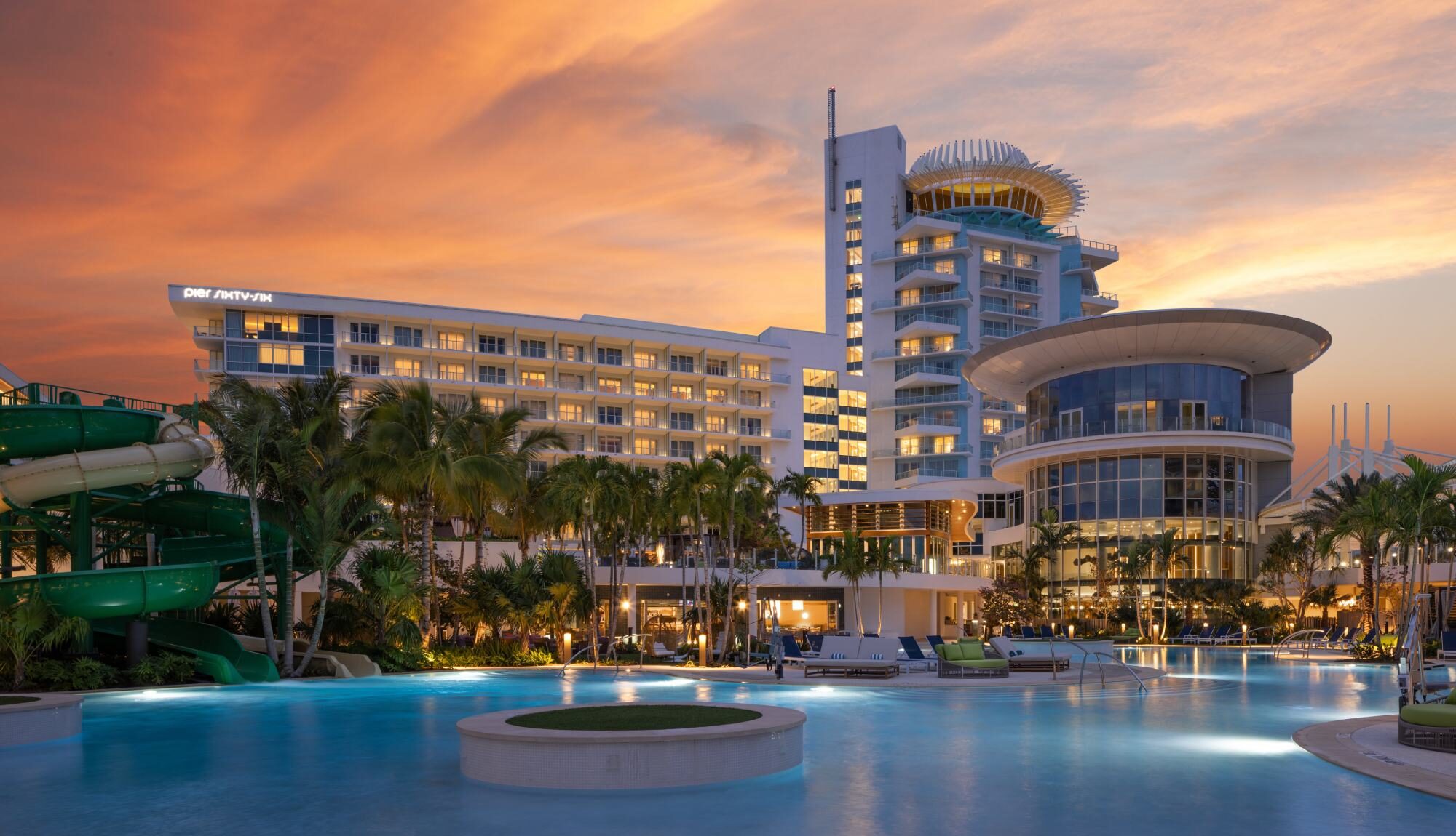 Sunset-lit resort with a large pool, palm trees, and a modern multi-story hotel building.